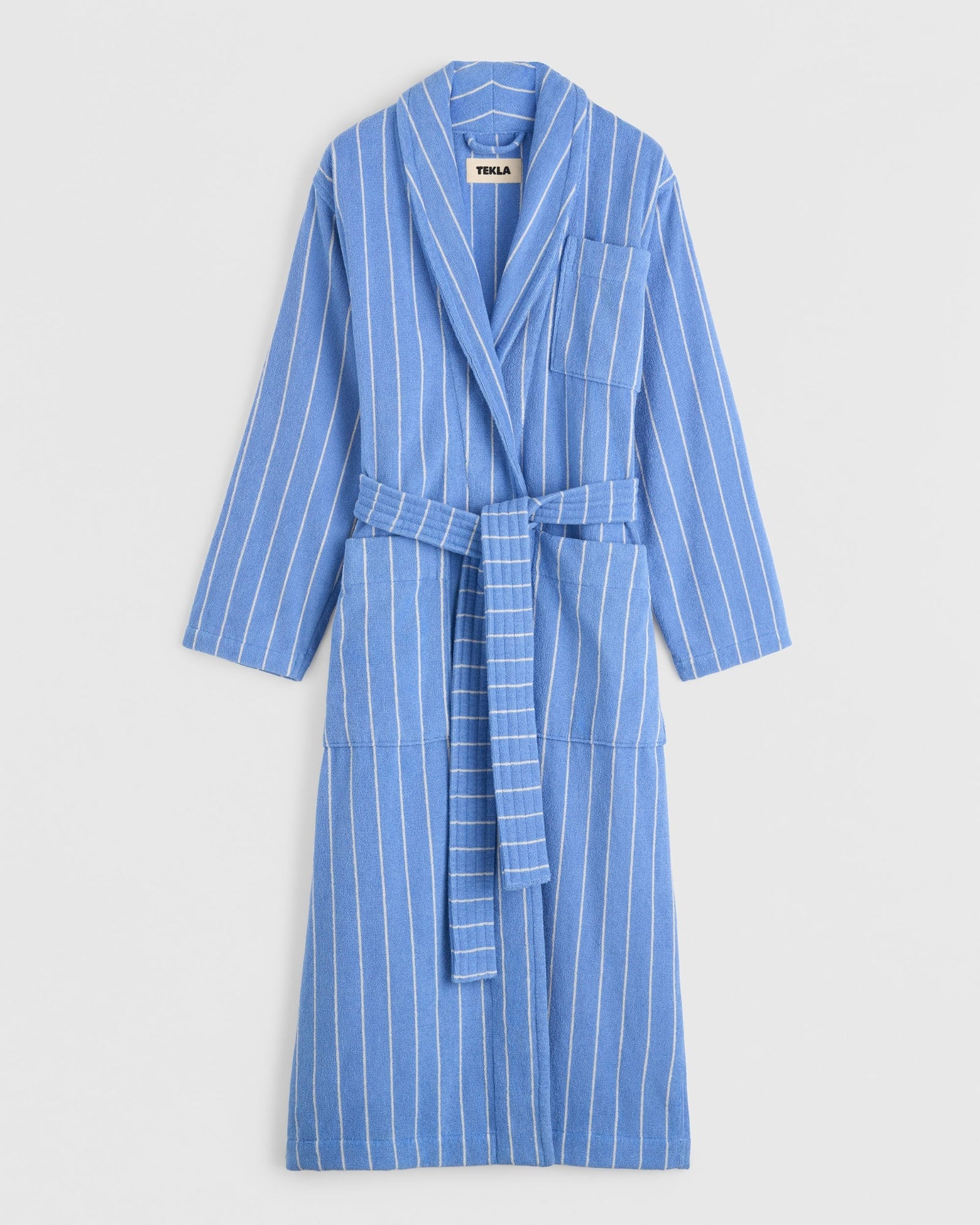 The TEKLA Classic Bathrobe in Marseille features blue and white stripes, long sleeves, a waist belt, and a chest pocket. Made from 100% organic cotton, it's shown against a plain white background.