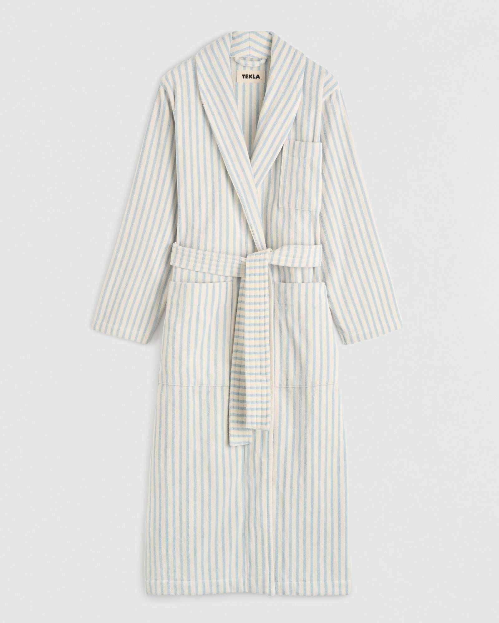 The TEKLA Classic Bathrobe in Soft Blue Stripes, made from organic cotton, features a collar, front and side pockets, and a matching waist belt, shown against a plain white background.