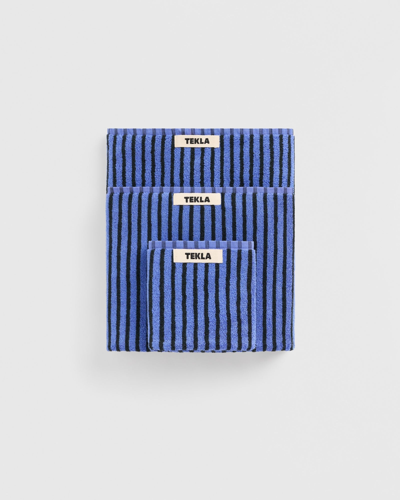 The TEKLA Towel Bundle in Black/Blue includes three organic cotton towels, stacked by size against a white background. Made in Portugal, their rich texture and quality craftsmanship are clearly visible.