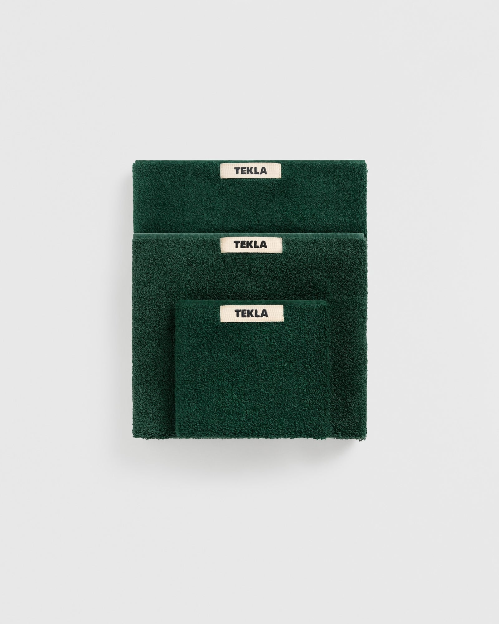 The TEKLA Towel Bundle in Forest Green features three neatly stacked organic cotton towels, each with a beige TEKLA label, set against a plain white background.