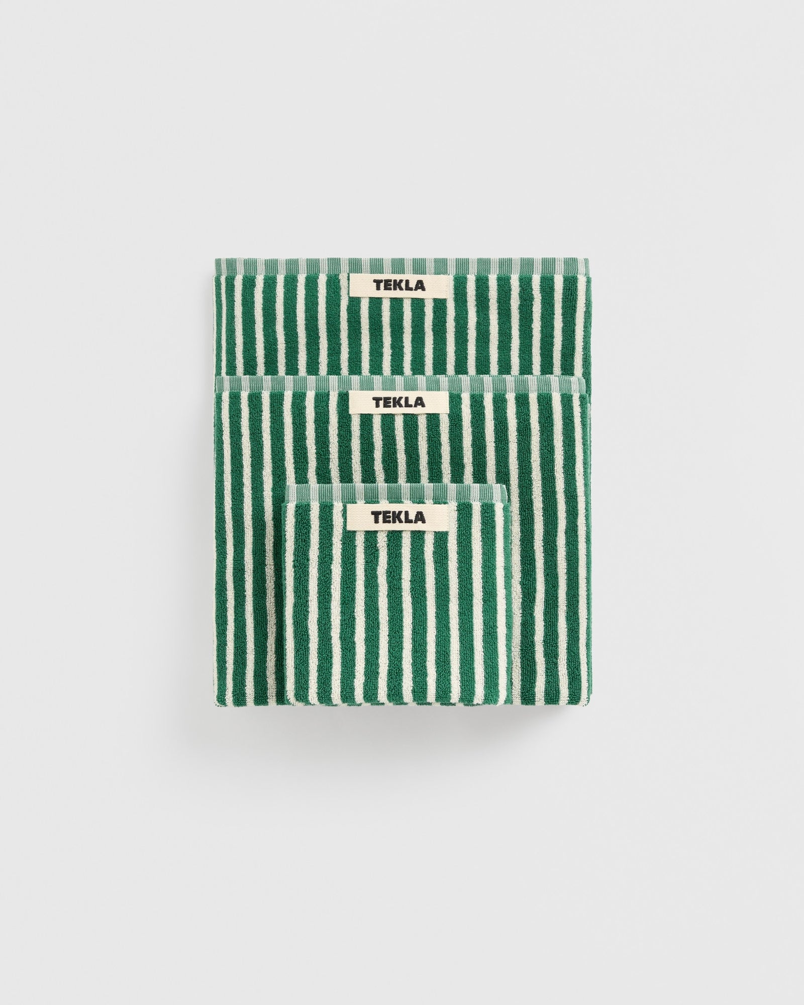 Three neatly stacked TEKLA Towel Bundle in Teal Green Stripes, each made from organic cotton and featuring branded labels, is displayed against a plain white background.
