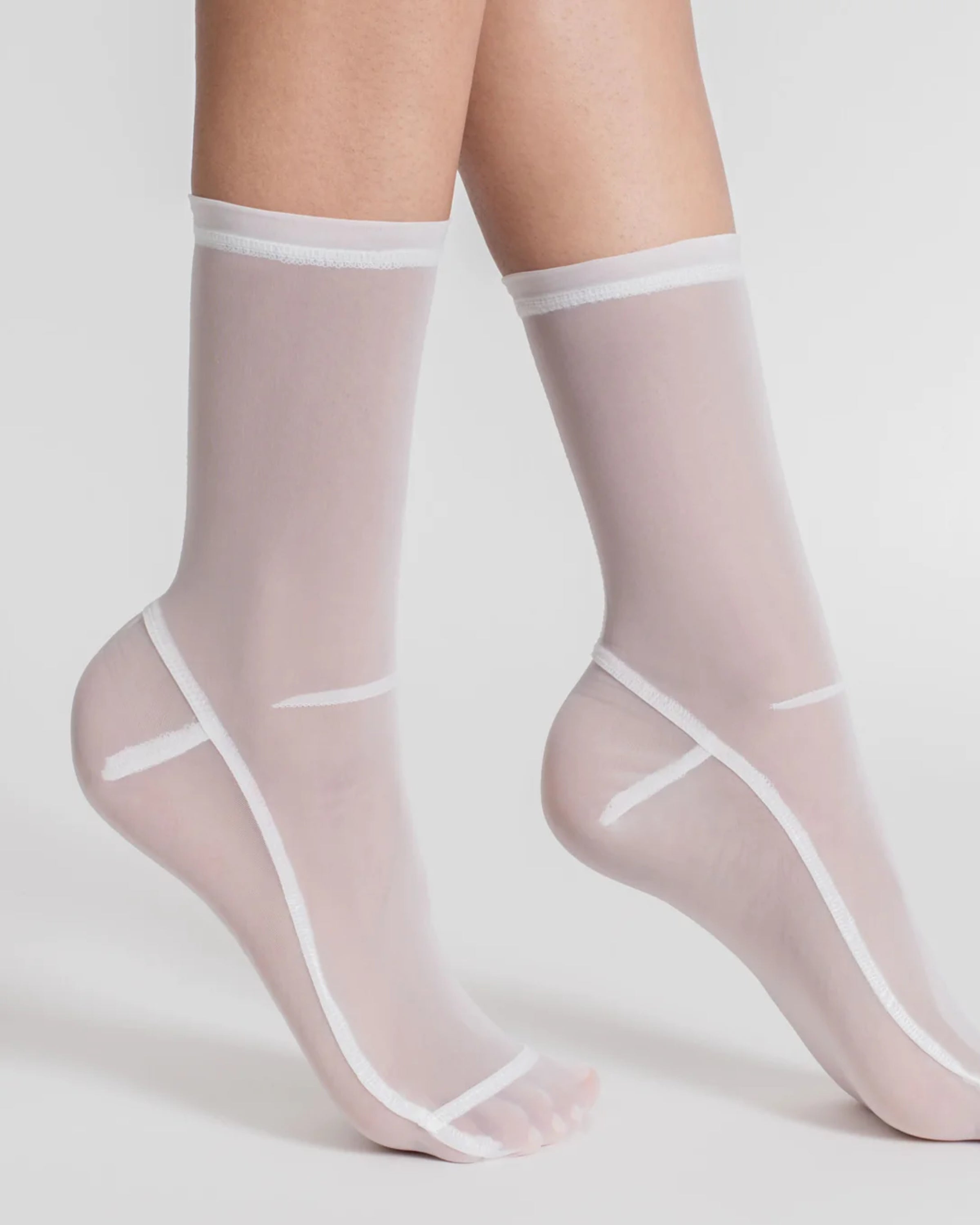 A person wears Darner Solid Mesh Socks in White featuring sheer fabric and distinctive white seams along the toes, sides, and tops, standing against a white background.