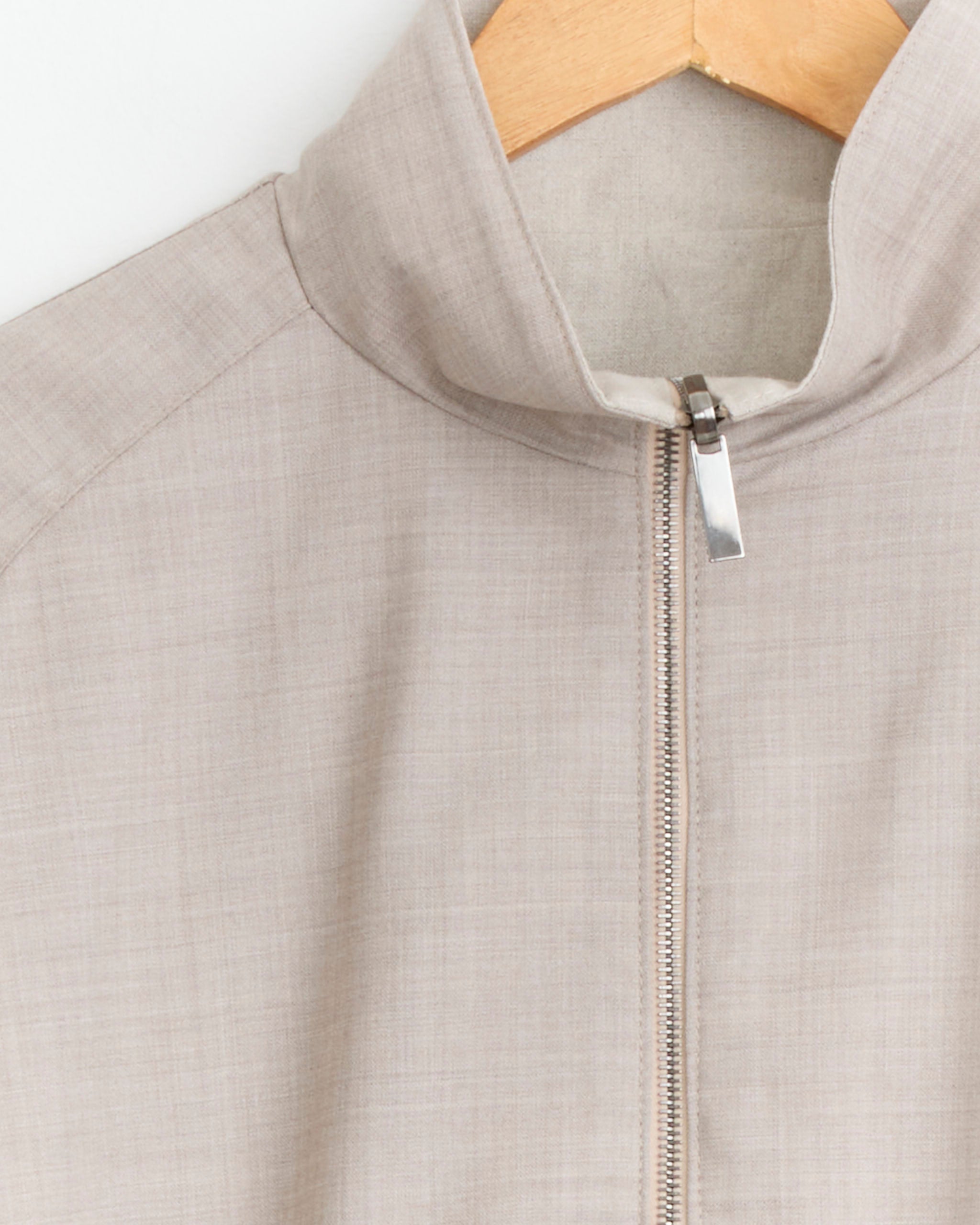 The Stoffa Reversible Blouson in Taupe, featuring a high collar and metallic zipper, hangs on a wooden hanger against a white background.
