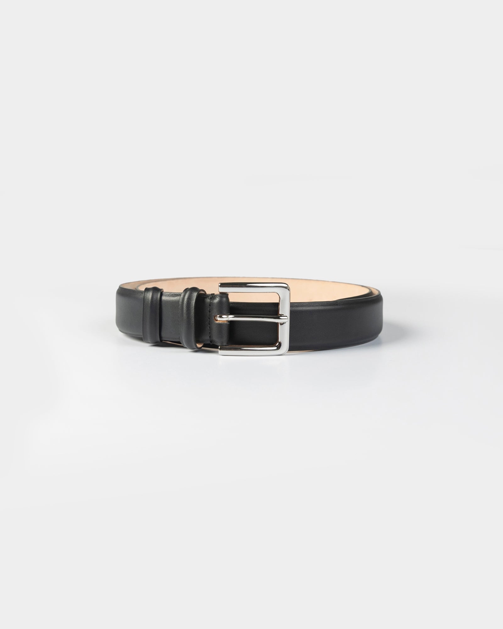 The CORDERA Classic Belt in Black, crafted from smooth calfskin and finished with a polished silver buckle, is coiled neatly on a plain white background.
