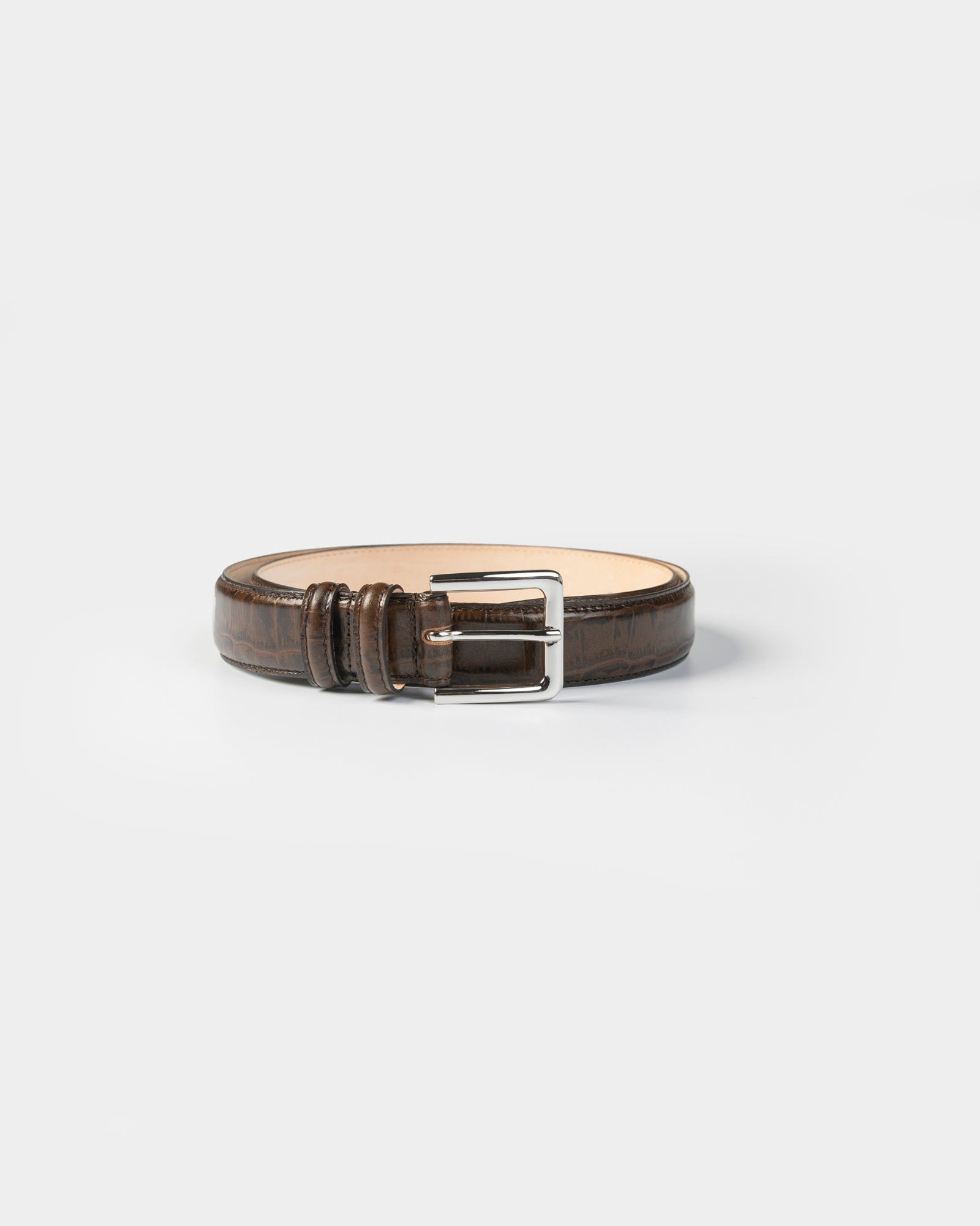 The CORDERA Classic Crocodile Belt in Brown, featuring a silver rectangular buckle, is coiled neatly on a plain white background.