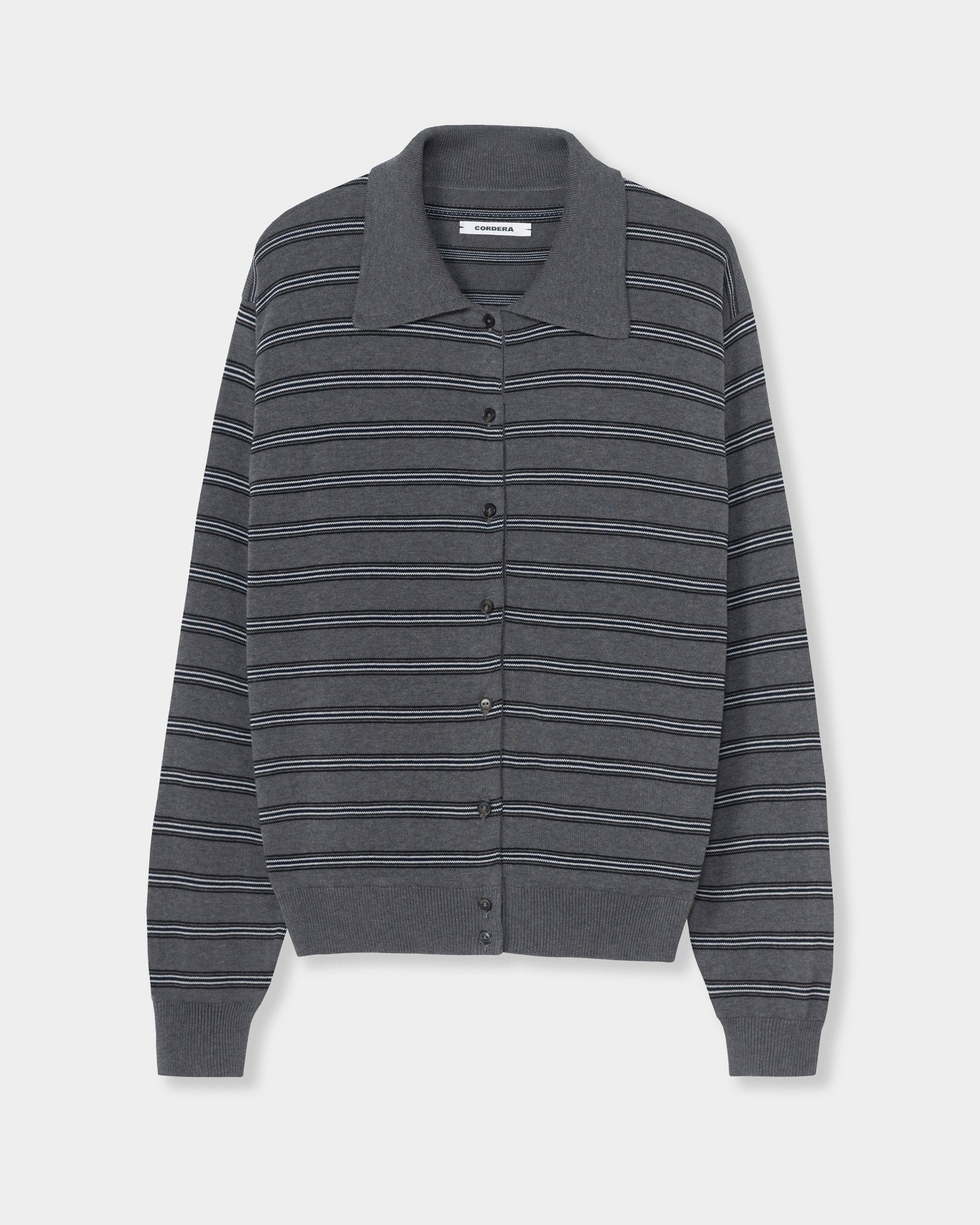 The Striped Polo Cardigan in Grey by CORDERA is an organic cotton button-up sweater with a collar and long sleeves, featuring thin horizontal stripes in white and light blue. This cardigan is designed with ribbed cuffs and hem, and is shown against a plain white background.