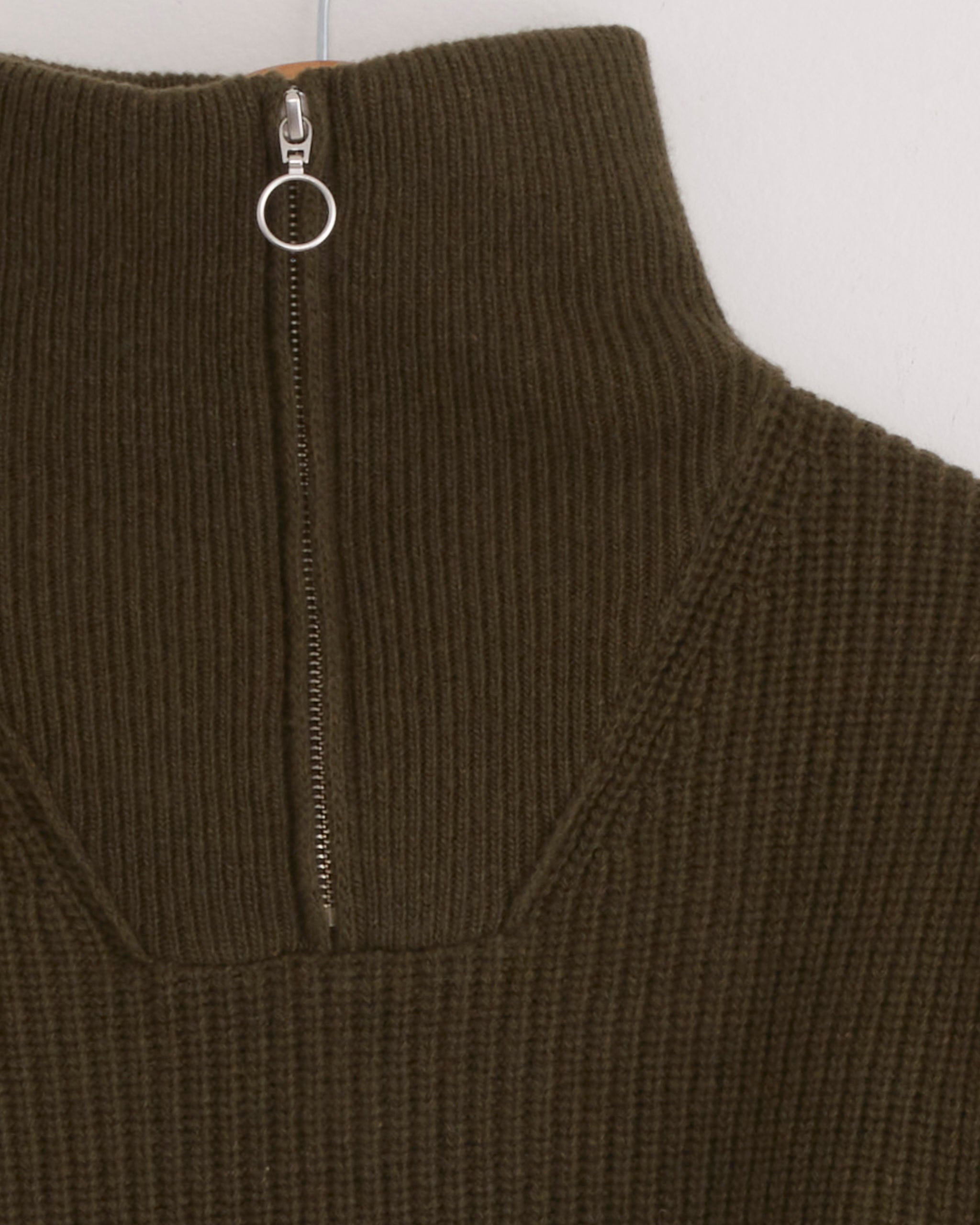 Close-up of the Fly Deck Sweater in Canteen by Girls of Dust, a ribbed merino wool sweater in olive green, featuring a high collar and a silver zipper with a circular pull tab.