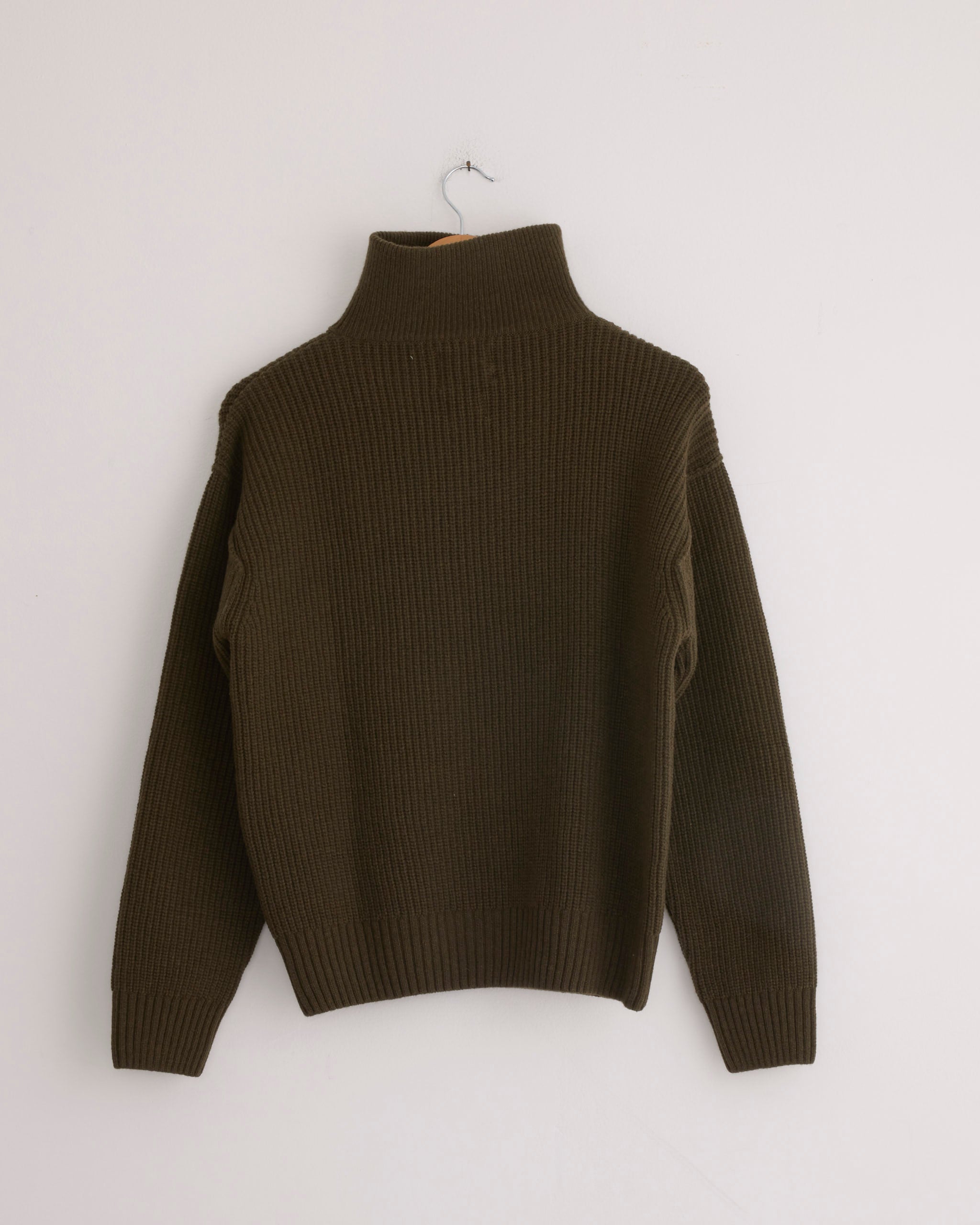 The Girls of Dust Fly Deck Sweater in Canteen, crafted from merino wool, hangs on a metal hanger against a plain white wall.