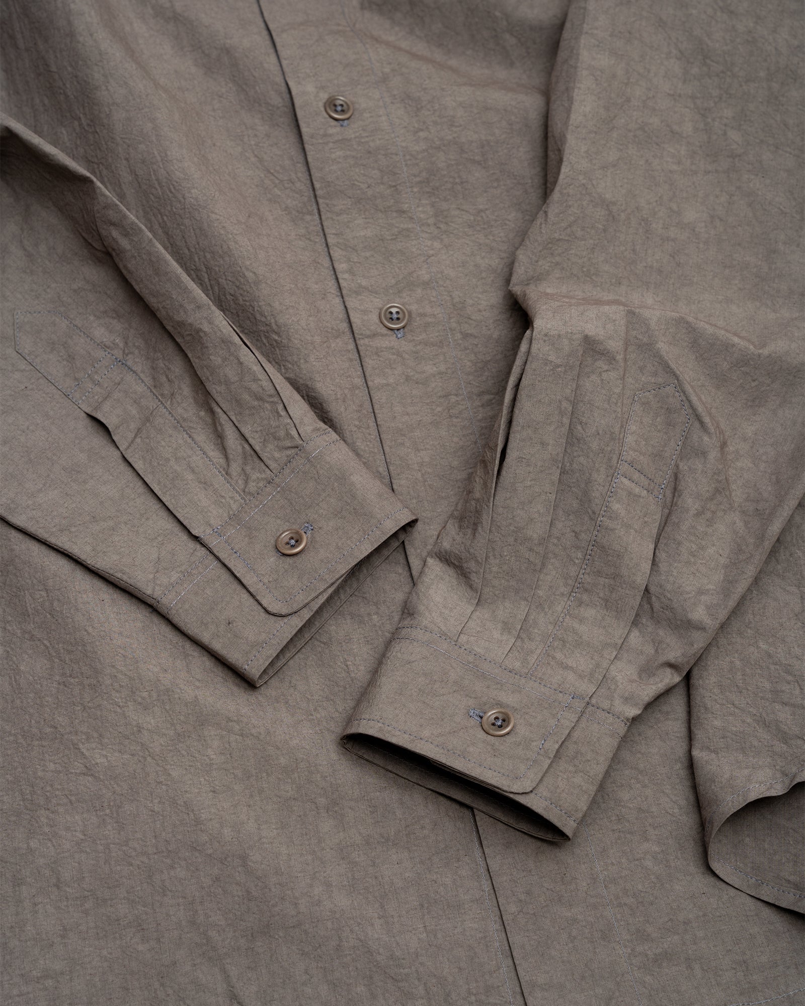 Close-up of a crinkled grey James Coward Filter Shirt made from Japanese typewriter cloth, featuring visible buttons and stitching on the cuffs and front placket, laid flat on a surface.