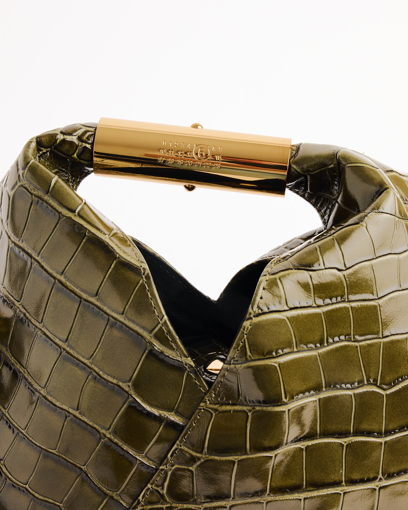 Close-up of the Japanese Small Bag in Olive by MM6 Maison Margiela, featuring a crocodile print and shiny gold metal handle with engraved branding, shown against a plain white background.