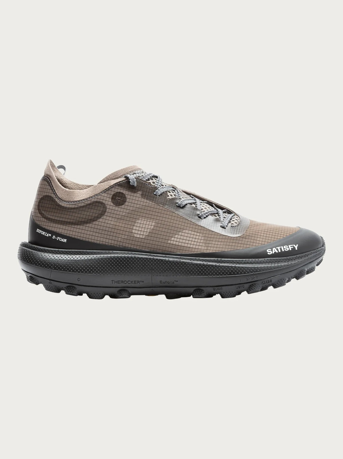 The Rocker in Falcon by Satisfy Running is a brown and black trail shoe with a textured Vibram Megagrip sole, gray laces, “SATISFY” on the toe, mesh upper with subtle pattern, branding by the heel and sole, and cushioned comfort for any terrain.
