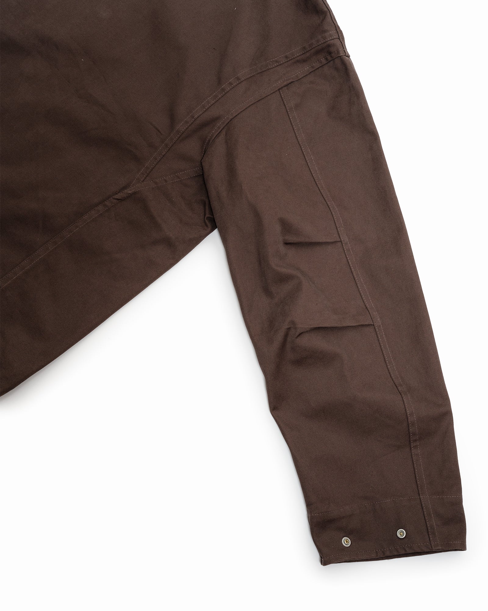 A close-up of the James Coward Six Jacket in Brown, a long-sleeve wading jacket made in Vancouver. The upper half and right sleeve highlight British cotton canvas, visible stitching, a pocket, and two metallic snap buttons at the cuff.