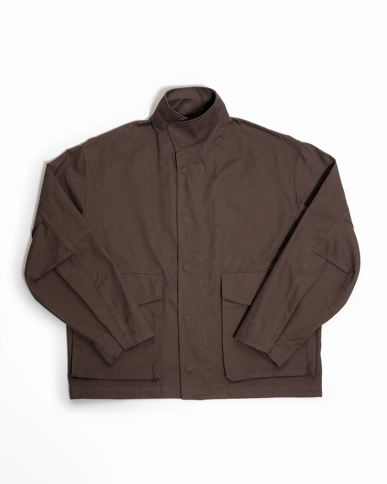 The Six Jacket in Brown by James Coward is a long-sleeve, collared wading jacket made from British cotton canvas, featuring a high neck, front placket, and two large front pockets, shown laid flat on a white background.