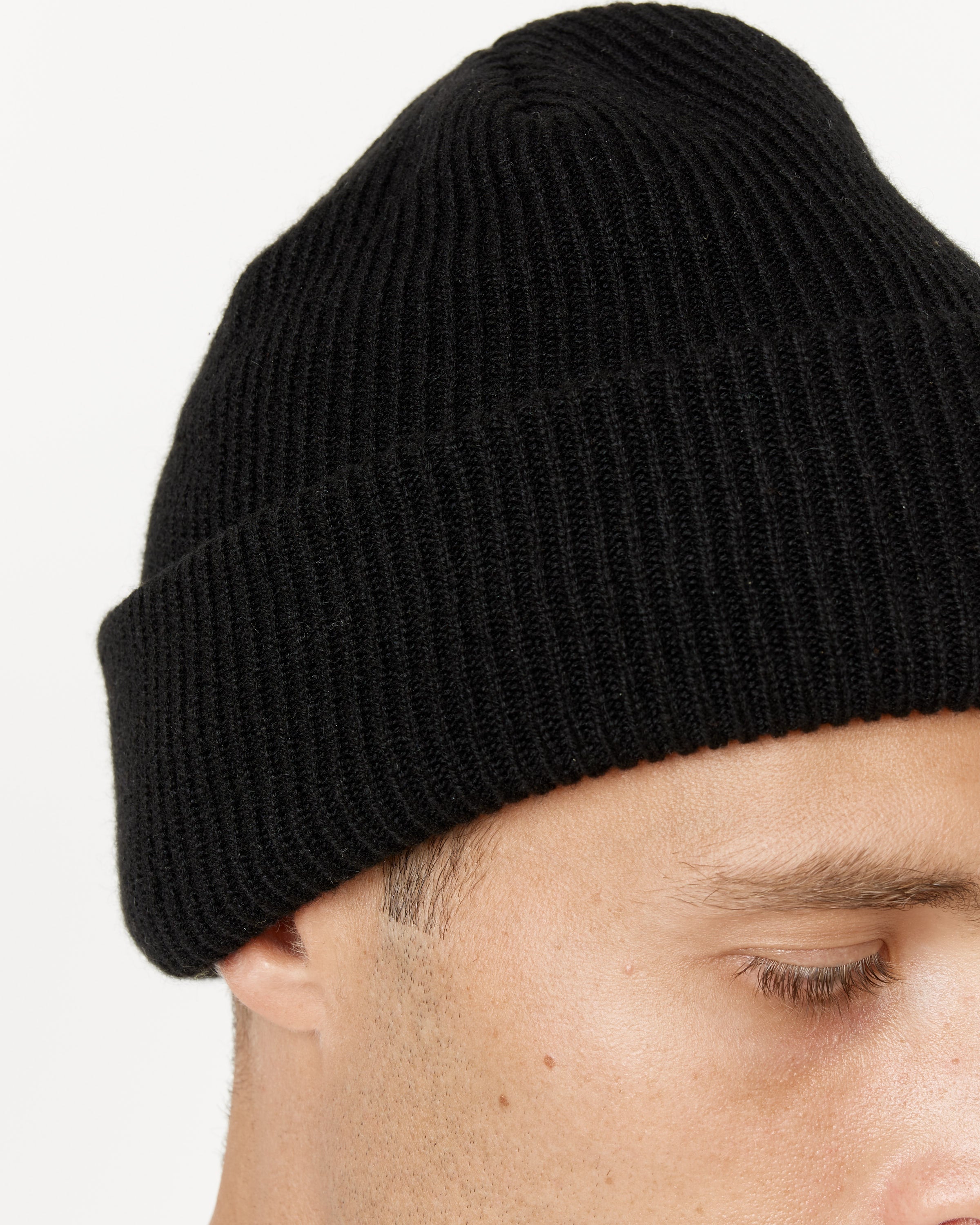 Close-up of a person wearing the SMOCK Cashmere Beanie in Black, with only their forehead and closed eye visible against a plain white background.