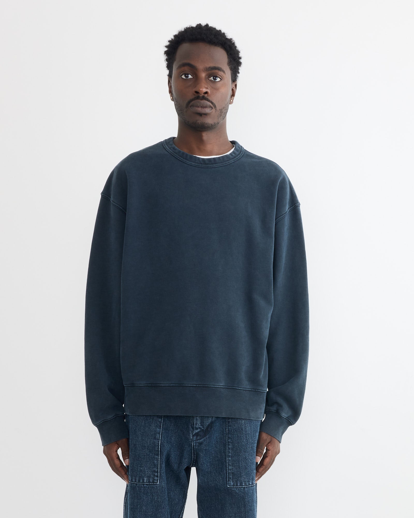 A man stands against a plain white background wearing the SMOCK Dolphy Crew in 22oz French Terry Navy and blue jeans. He faces forward with a neutral expression, his arms resting at his sides.