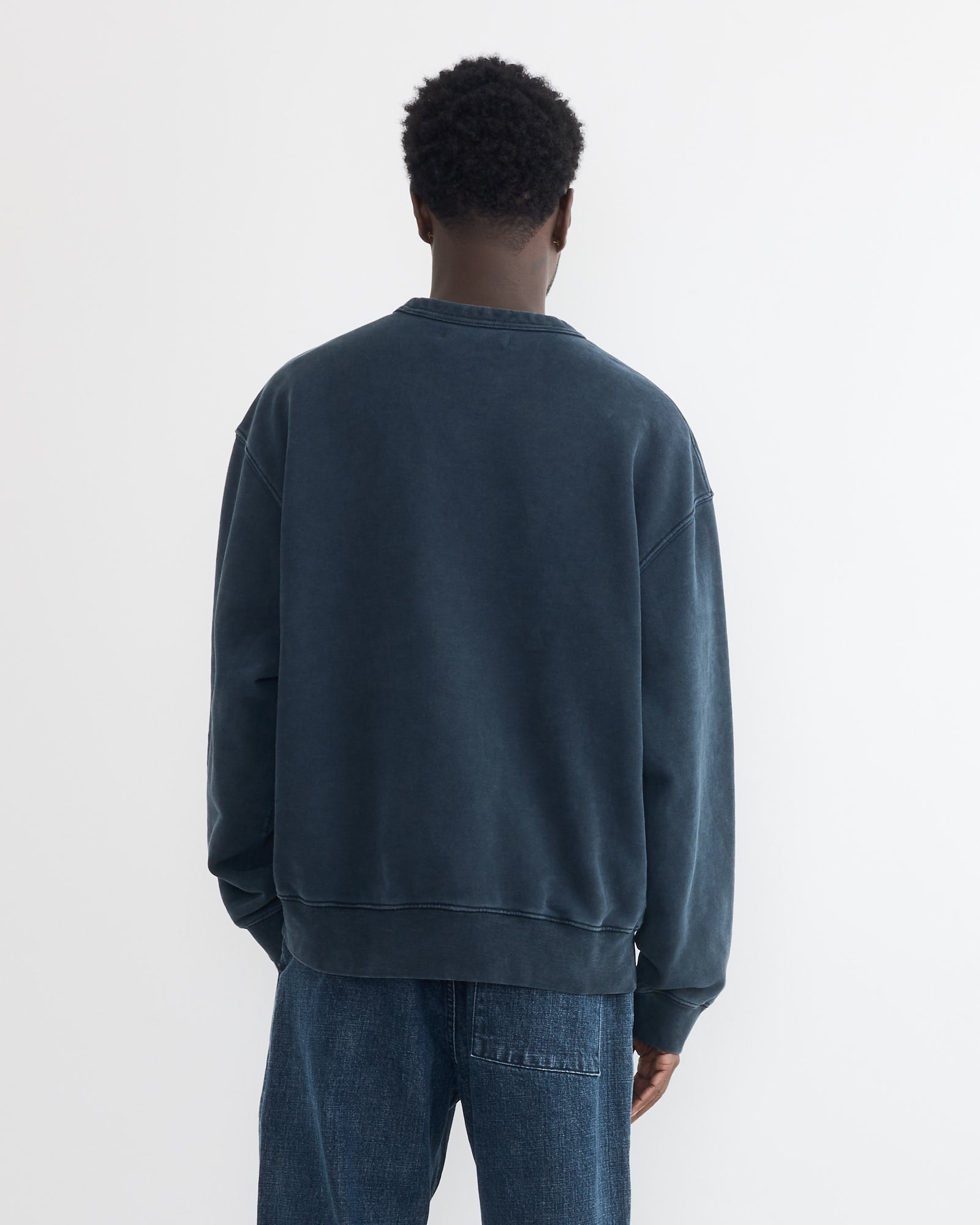 A person faces away from the camera, wearing the SMOCK Dolphy Crew in 22oz French Terry Navy and loose blue jeans, set against a plain white background.