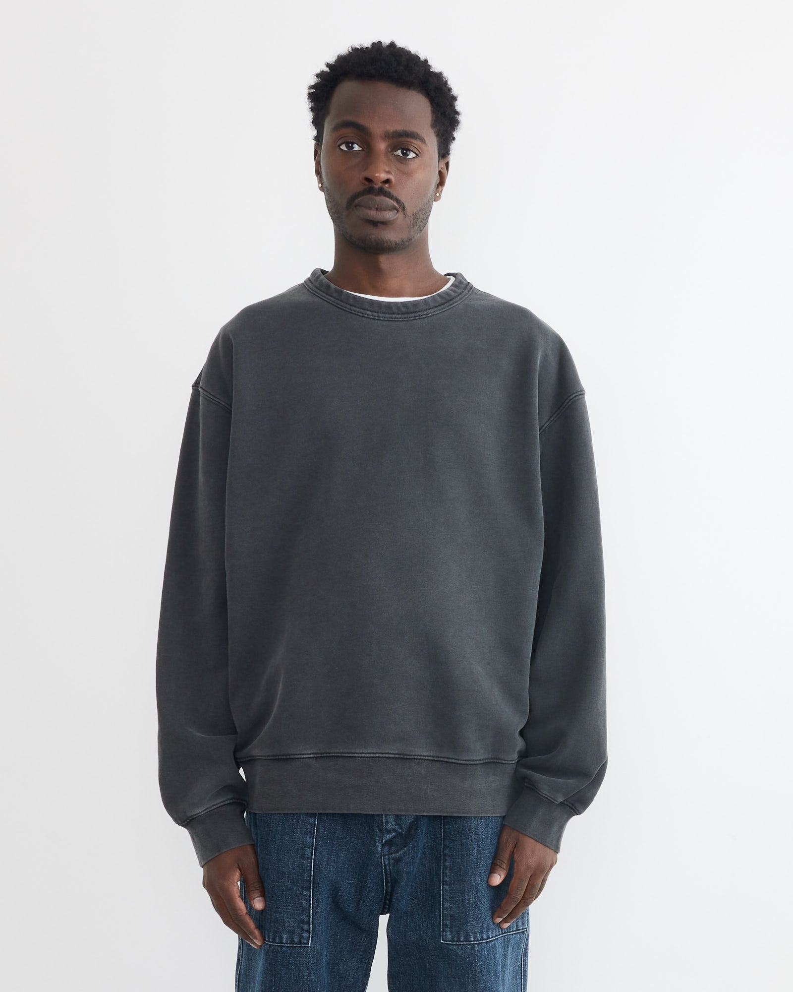 A man stands against a plain white background, wearing the SMOCK Dolphy Crew in 22oz French Terry Grey and blue jeans. He faces forward with relaxed arms, showcasing an effortless look made in Los Angeles.