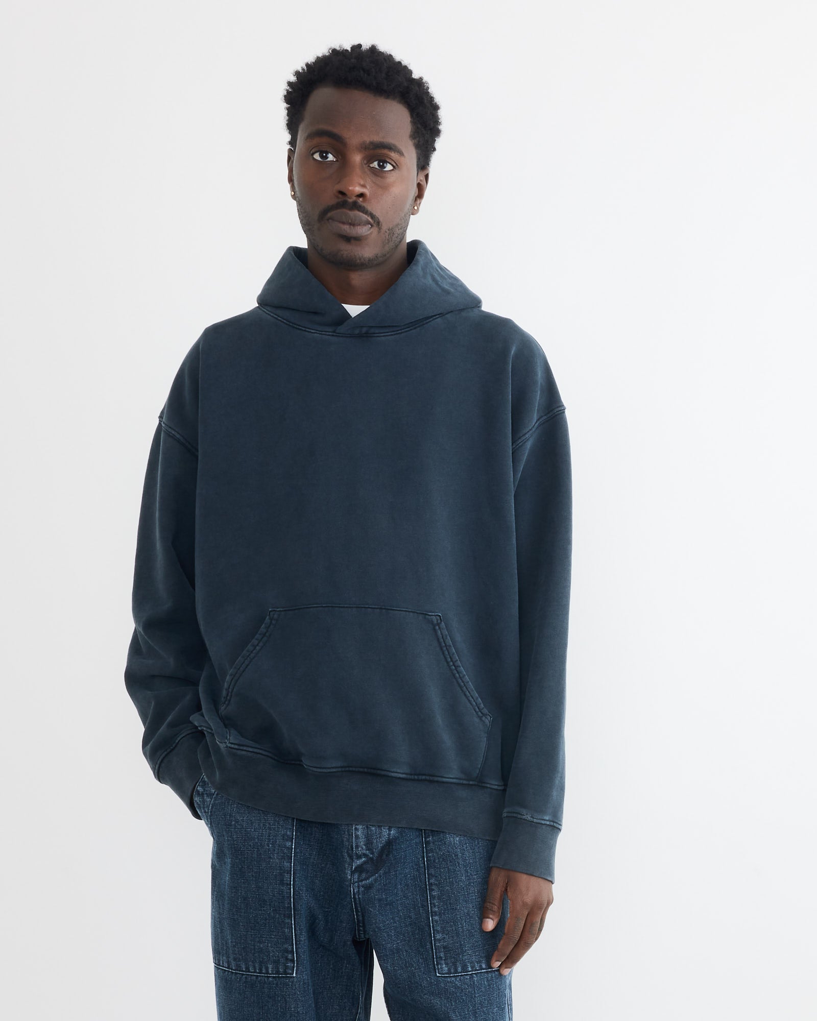 A person stands against a plain white background wearing the SMOCK Ornette Hoodie in 22oz French Terry Navy and blue jeans, looking directly at the camera with a neutral expression. Made in Los Angeles.
