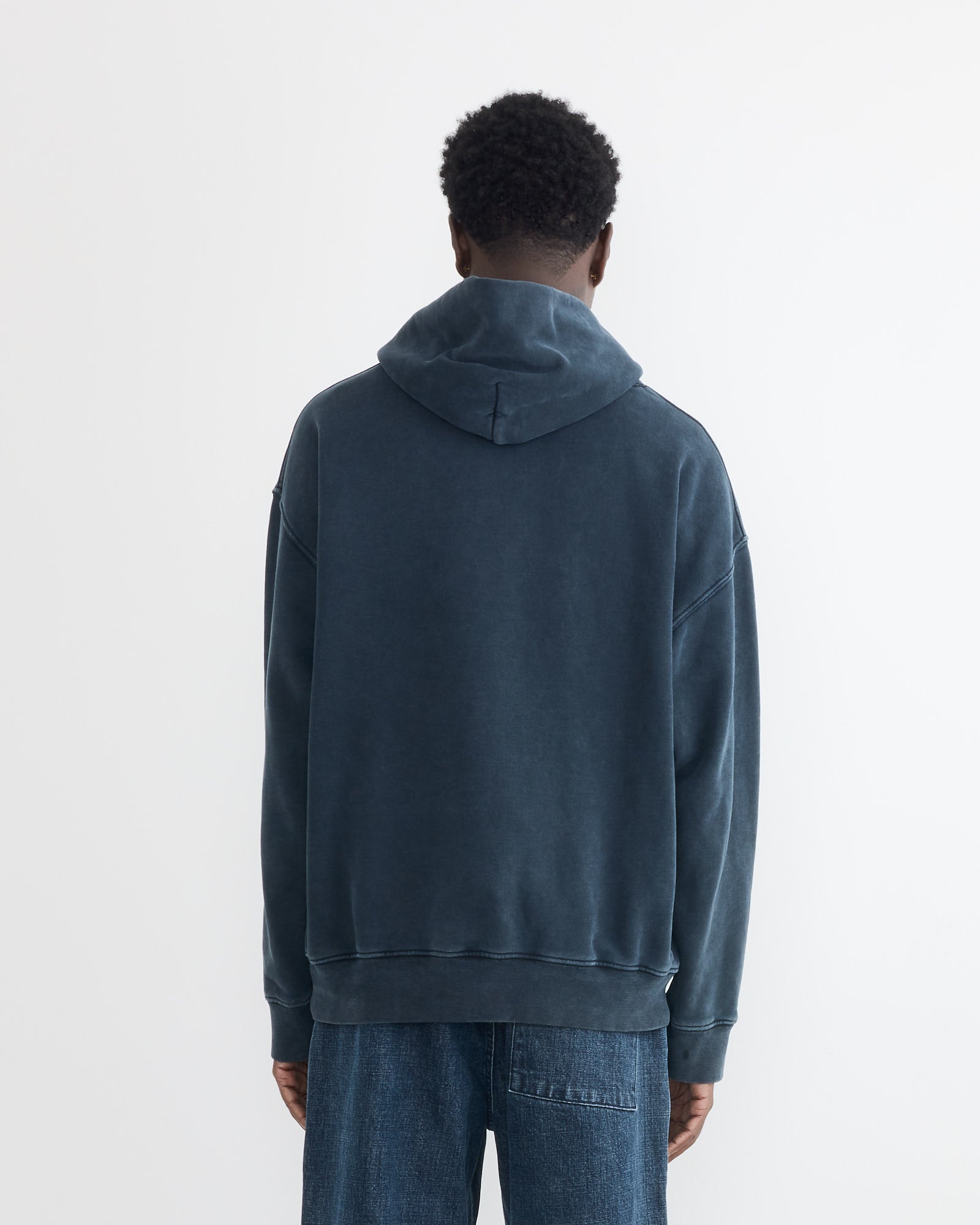 A person faces away from the camera, wearing the SMOCK Ornette Hoodie in 22oz French Terry Navy and blue jeans, set against a plain white background.