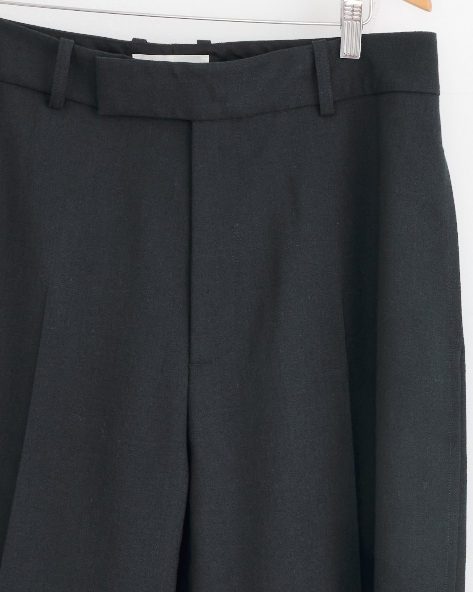 Close-up of Studio Nicholson’s Ester Pant in Darkest Navy, a tailored wool trouser made from Italian-milled grain de poudre, shown hanging with visible waistband, belt loops, and front pleats against a plain white background.