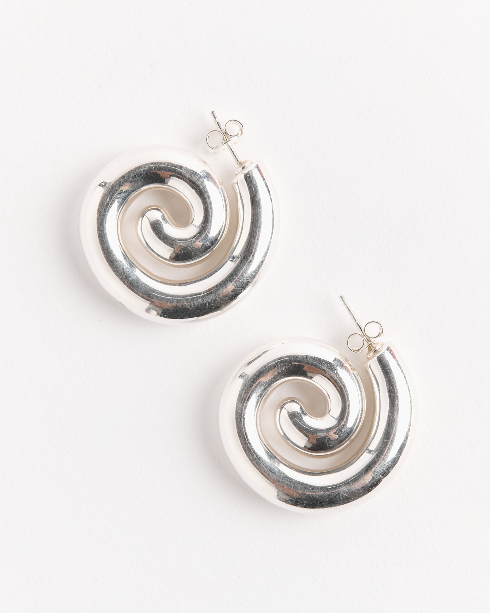 The NOMIA Spiral Earrings are shiny Sterling Silver studs with spiral shapes and butterfly backings—perfect minimalist jewelry, shown on a white background.