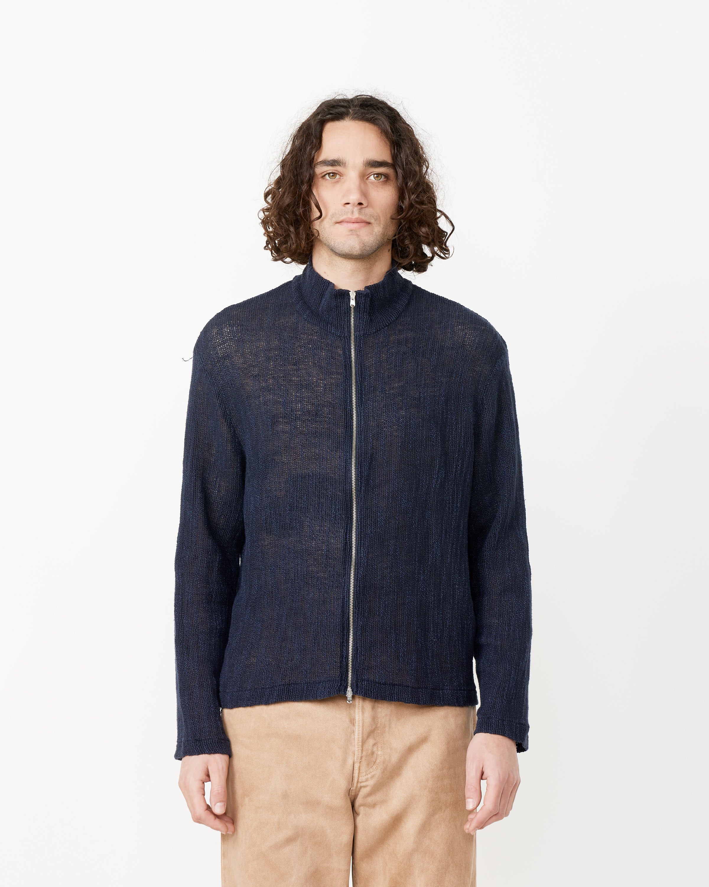 A person with curly hair wears the Our Legacy Shrunken Fullzip Polo in navy with a boxy fit, paired with beige pants, against a plain white background.
