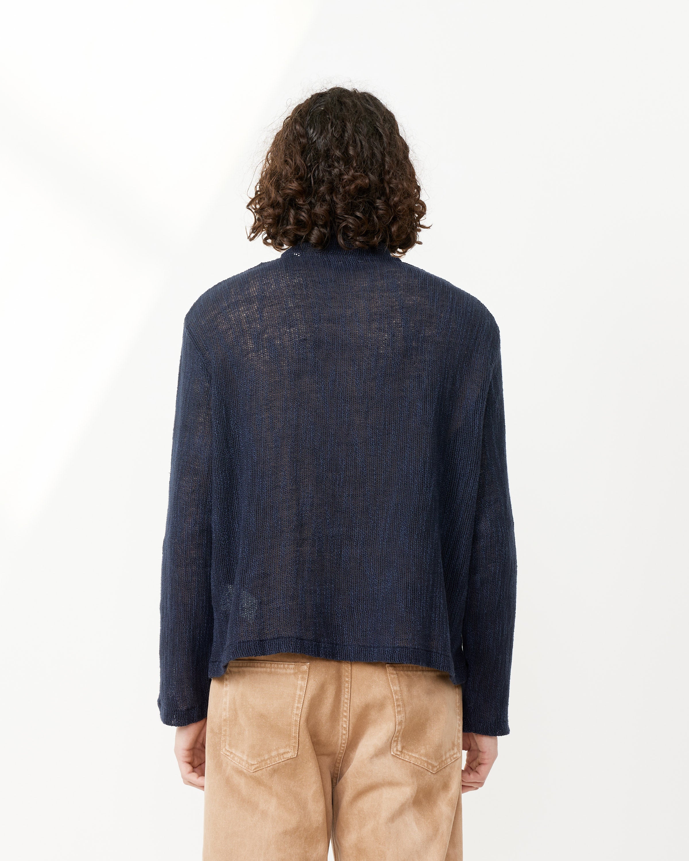 A person with curly hair is shown from the back, wearing the Shrunken Fullzip Polo by Our Legacy and light brown pants, standing against a plain white background.