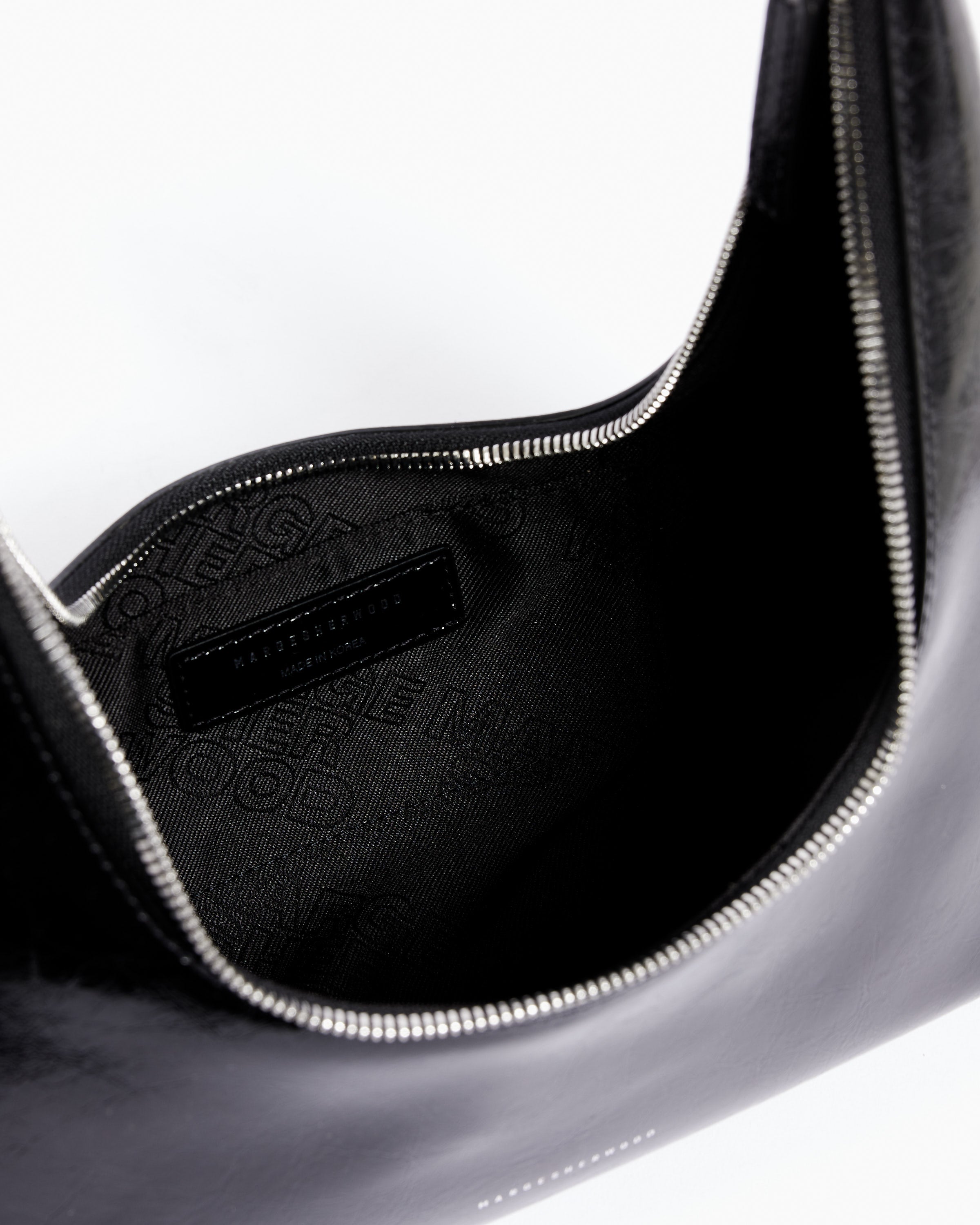 A close-up of the open Marge Sherwood Hobo Shoulder Bag - Black Crinkle highlights its Italian cowhide leather, silver zipper, and fabric lining with subtle embossed text.