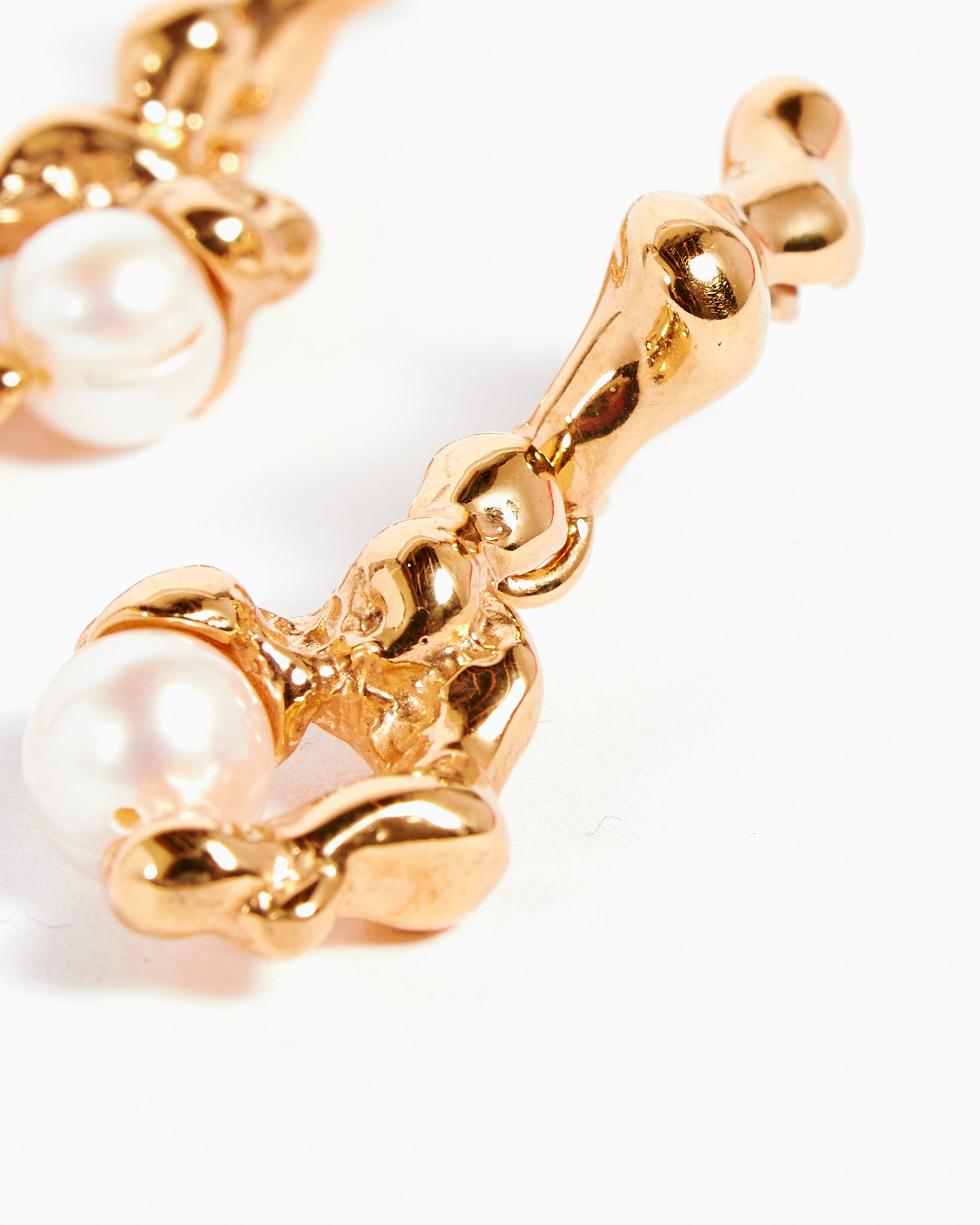 Close-up of Faris 18K Gold Plated Fellini Drops, handcrafted earrings with an organic sculpted design featuring a round white pearl set in gold. The white background accentuates their shiny, textured finish.