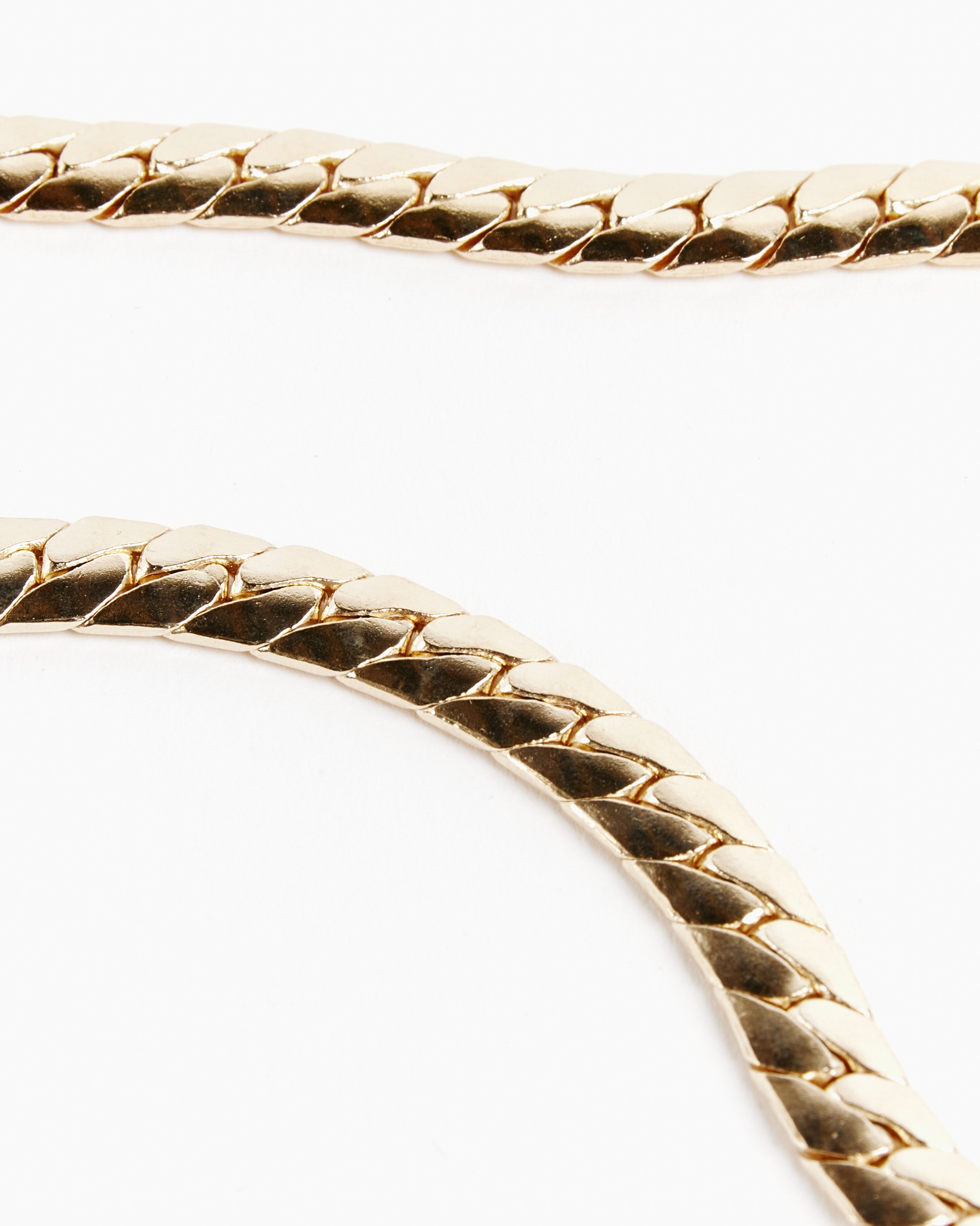 Close-up of two Laura Lombardi 14K Gold Plated Brass Piatta Chain Necklaces, featuring a flat, interlocking herringbone pattern, arranged diagonally on a plain white background.